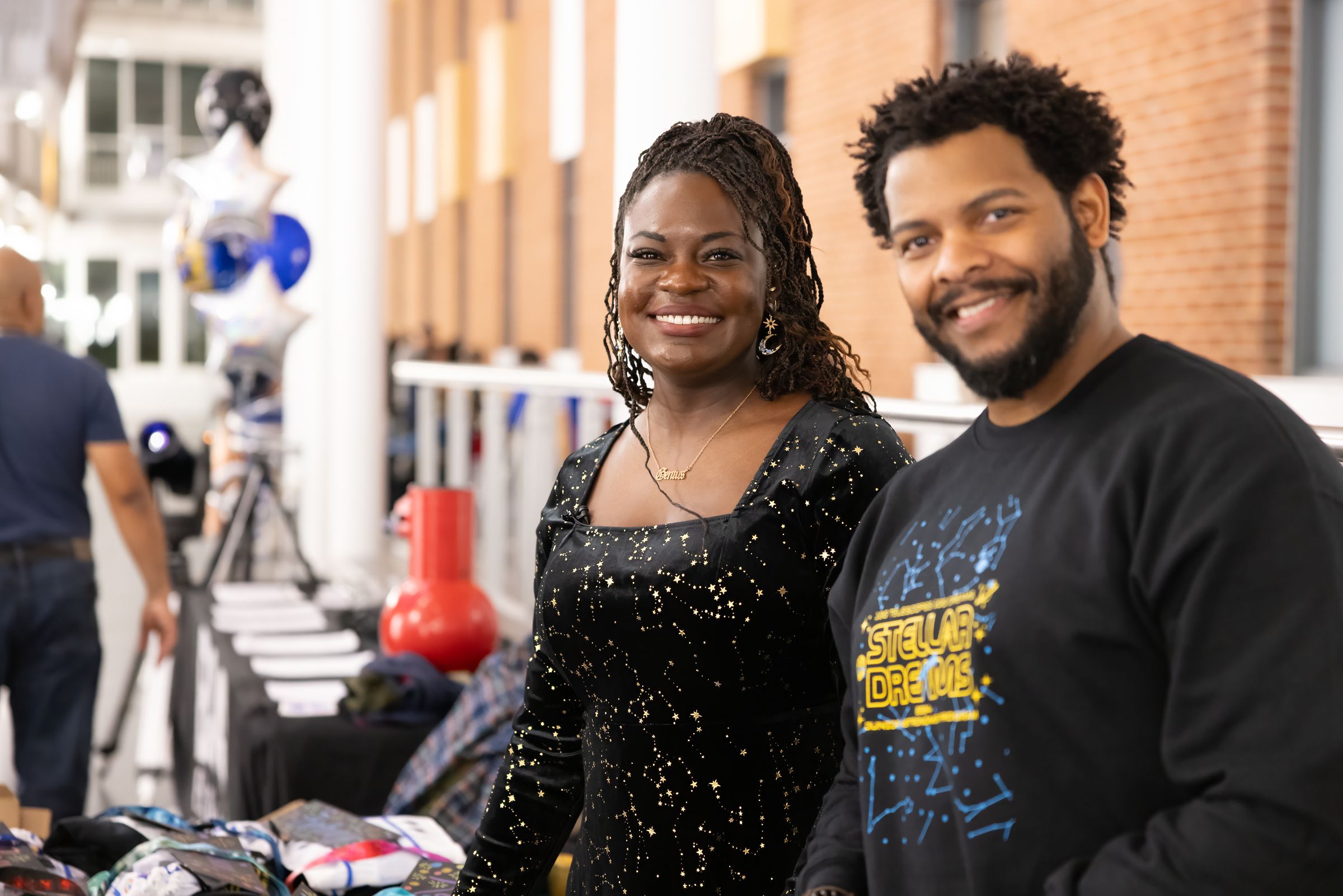 Dr. Raven Baxter and Dr. Ronald Gamble smile at the camera behind the gift bag table in the atrium