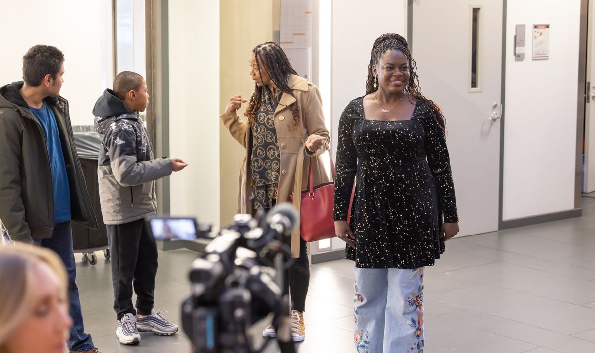 Dr. Raven Baxter walks down a hallway in the Science and Mathematics Complex past arriving guests, with a video camera in the foreground