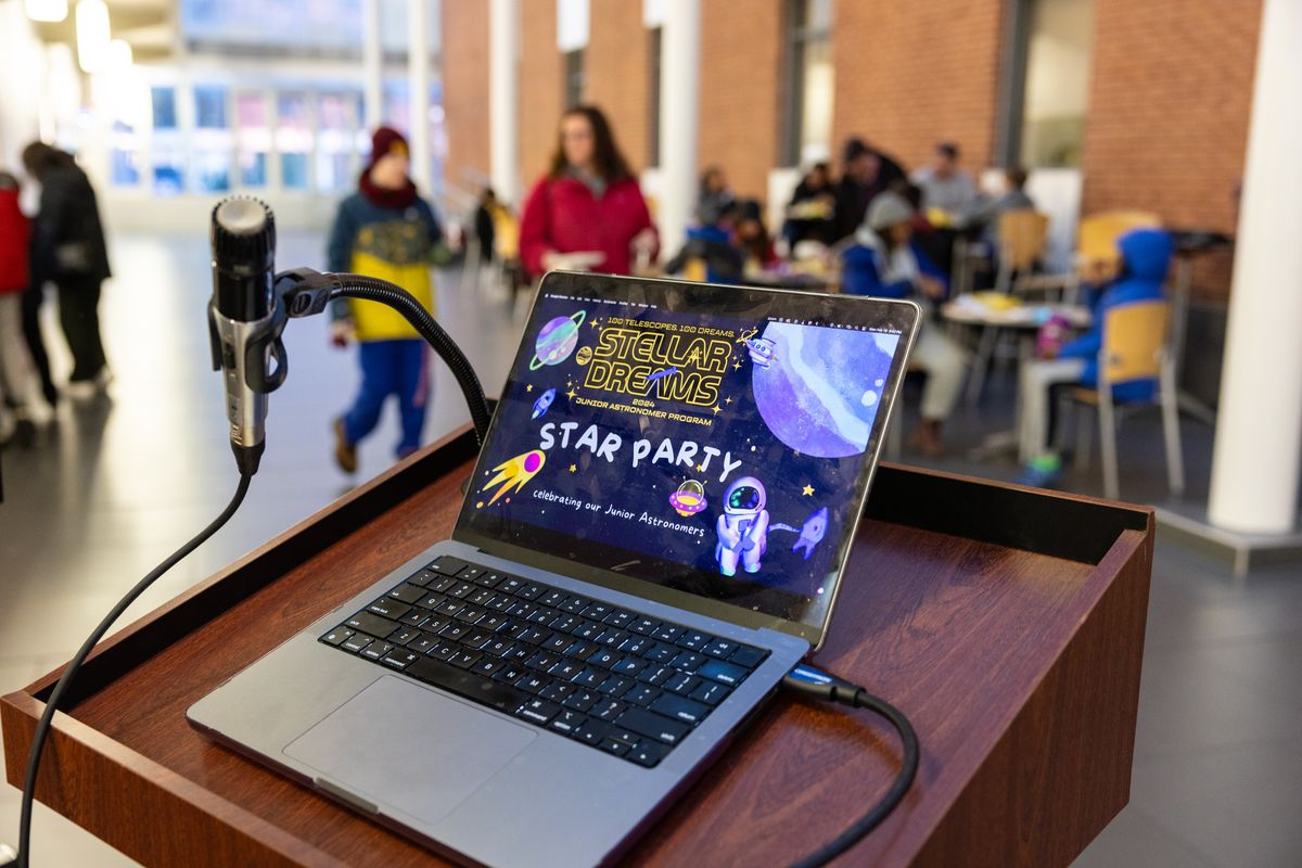 A laptop on the podium shows the Stellar Dreams Star Party title slide while guests eat at tables behind it
