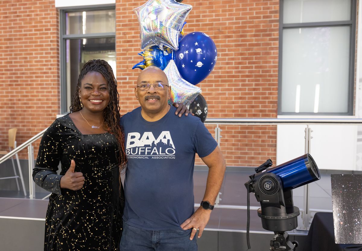 Dr. Raven Baxter gives a thumbs up beside Michael Humphrey, in a Buffalo Astronomical Association shirt, and a demonstration telescope