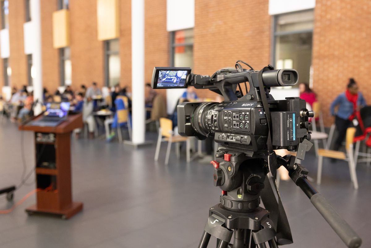 A video camera on a tripod faces the Buffalo State podium while guests eat at tables in the atrium