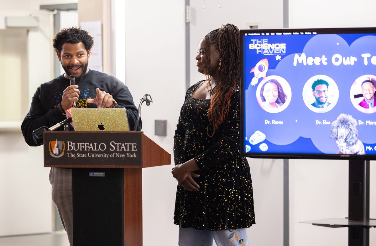 Dr. Ronald Gamble speaks at the podium as Dr. Raven Baxter looks on beside a Meet Our Team slide