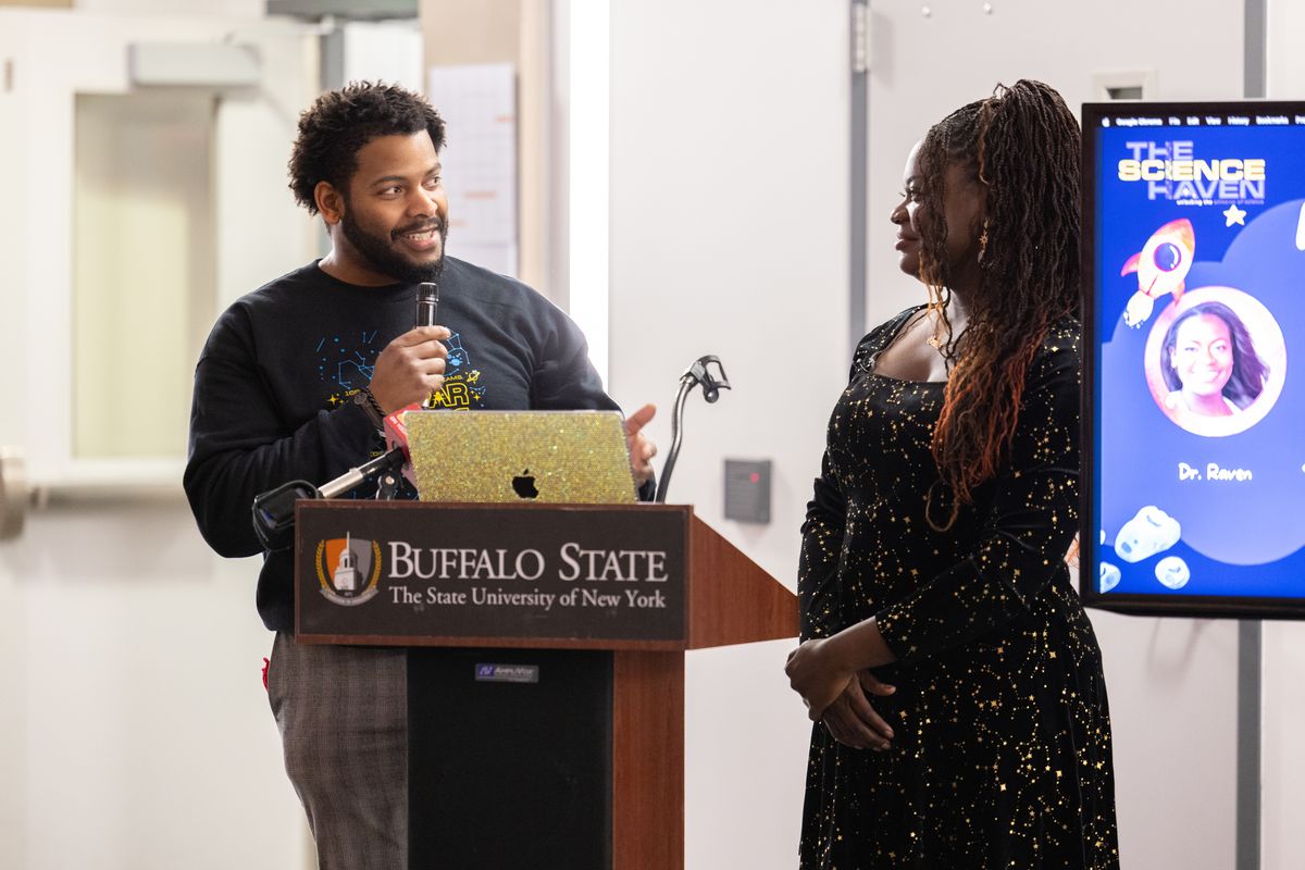 Dr. Ronald Gamble speaks at the Buffalo State podium while Dr. Raven Baxter listens beside a Science Haven slide