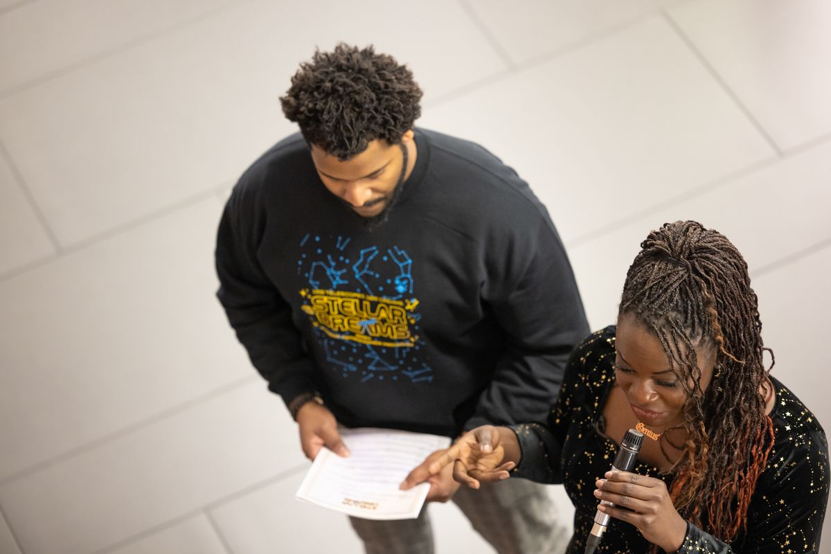 Close overhead view of Dr. Raven Baxter pointing to the printed program held by Dr. Ronald Gamble as she speaks