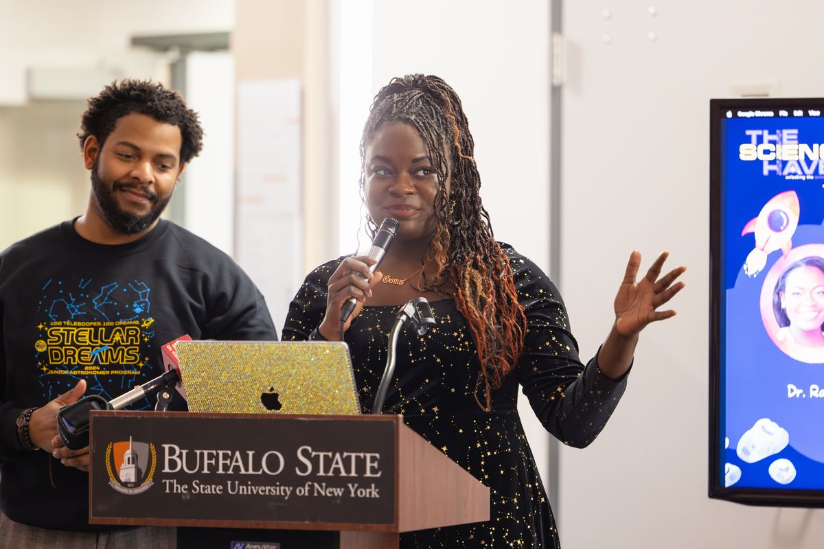 Dr. Raven Baxter gestures as she speaks at the Buffalo State podium, with Dr. Ronald Gamble smiling beside her