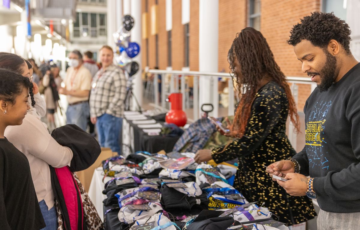 Dr. Raven Baxter and Dr. Ronald Gamble sort gift bags and cards at a long table as students and parents line up
