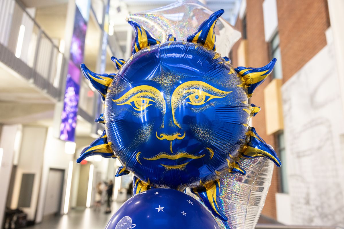 Close view of a blue sun face balloon with gold rays among silver star balloons in the atrium